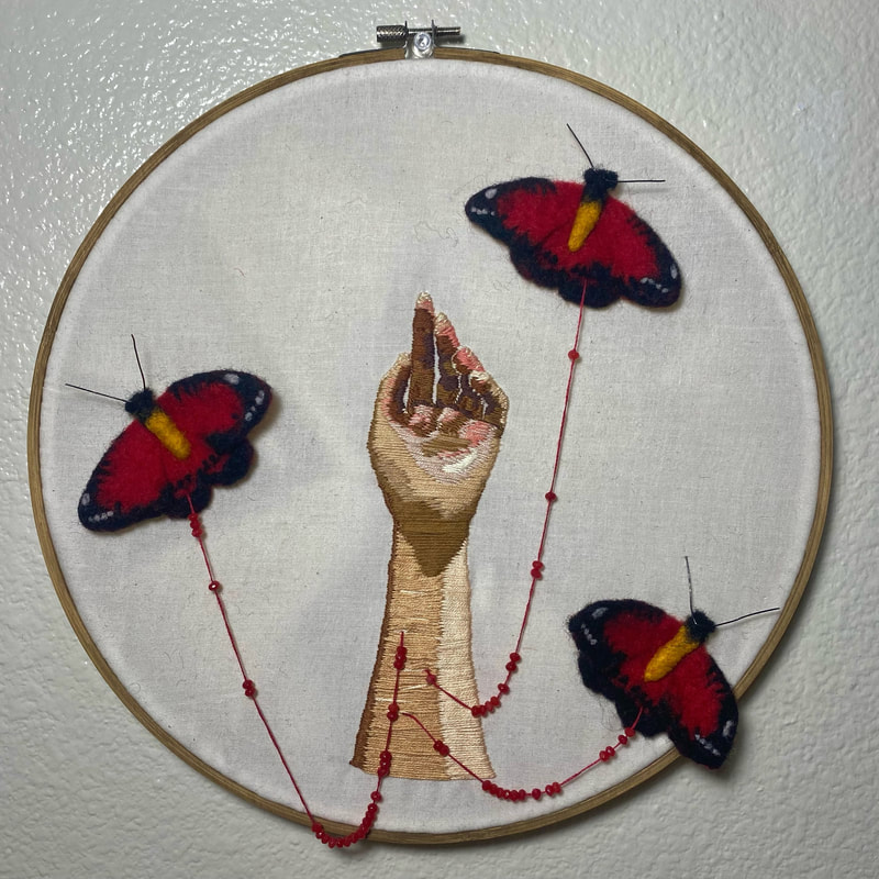 Picture An embroidered hand with small scars on the arm on a white background in a wooden hoop. Red threads with beads extend from the scars and turn into red and black felt butterflies.